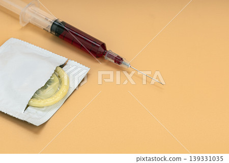 Open Condom Packet and Blood-Filled Medical Syringe Placed Together on Warm Orange Background Representing Sexual Health, HIV Transmission Risk, and STI Prevention Awareness Concept 139331035