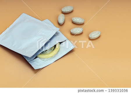 Open Condom Packets with Yellow Latex Condom and Scattered Beige Supplement Tablets on Warm Orange Background Representing Sexual Health and Safe Sex Awareness Open Condom Packets with Yellow Latex Condom and Scattered Beige Supplement Tablets on Warm Orange Background Representing Sexual Health and Safe Sex Awareness 139331036