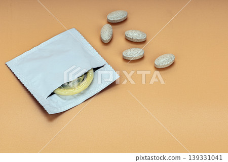 Open Torn Condom Wrapper with Yellow Condom and Scattered Beige Pills on Warm Tan Background Representing Sexual Health and Contraception Awareness Open Torn Condom Wrapper with Yellow Condom and Scattered Beige Pills on Warm Tan Background Representing Sexual Health and Contraception Awareness 139331041