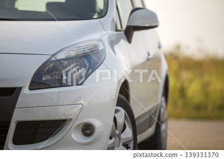 Close-up front view detail of silver new shiny luxurious car parked on field road on blurred summer sunny green grass and clear blue sky copy space background. Close-up front view detail of silver new shiny luxurious car parked on field road on blurred summer sunny green grass and clear blue sky copy space background. 139331370