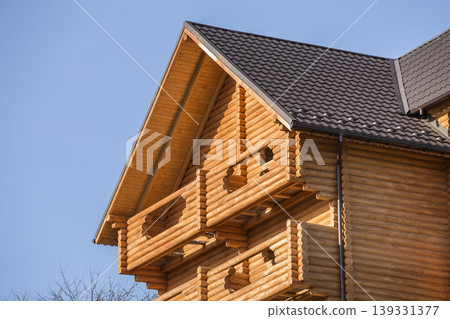 Close-up detail of new modern wooden warm ecological cottage house top with shingled brown roof and wooden sidings on blue sky background. Professionally done carpentry and construction work. 139331377