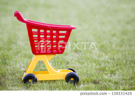 Bright plastic colorful shopping cart toy outdoors on sunny summer day. 139331420