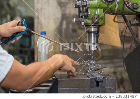 Skilled machine operator clearing spiral metal chips from an NC milling machine during drilling process. Skilled machine operator clearing spiral metal chips from an NC milling machine during drilling process. 139331487