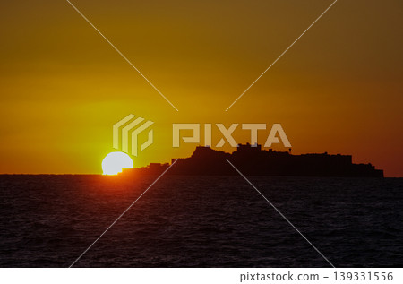 A breathtaking view of the silhouette of Gunkanjima (Hashima), a World Heritage site in Nagasaki Prefecture, and the vibrant sunset sinking below the horizon of the East China Sea. A breathtaking view of the silhouette of Gunkanjima (Hashima), a World Heritage site in Nagasaki Prefecture, and the vibrant sunset sinking below the horizon of the East China Sea. 139331556
