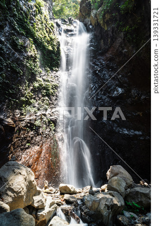 Tropical waterfall cascading over dark rocks with sunlight and mist creating a natural scene Tropical waterfall cascading over dark rocks with sunlight and mist creating a natural scene 139331721