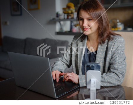 Mother working remotely from home, multitasking between professional tasks and family responsibilities, using a laptop in a cozy home environment. Mother working remotely from home, multitasking between professional tasks and family responsibilities, using a laptop in a cozy home environment. 139331772