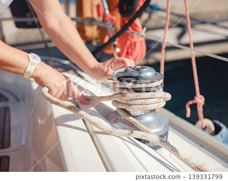 Detail view of hands working with nautical ropes and winches on sailing boat. Secure knotting and tension control are essential for safe mooring and sailing operations on yacht. Detail view of hands working with nautical ropes and winches on sailing boat. Secure knotting and tension control are essential for safe mooring and sailing operations on yacht. 139331799