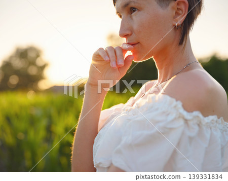 Beautiful woman in white dress standing in summer field during golden sunset in Croatia, warm sunlight, romantic evening mood, natural countryside atmosphere, soft wind and peaceful scene Beautiful woman in white dress standing in summer field during golden sunset in Croatia, warm sunlight, romantic evening mood, natural countryside atmosphere, soft wind and peaceful scene 139331834