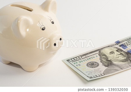 Piggy bank in the shape of a pig with 100 dollars lying next to it on a white background. Piggy bank in the shape of a pig with 100 dollars lying next to it on a white background. 139332030