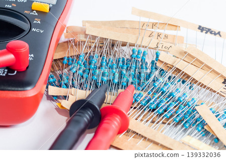 A multimeter with measurement probes and a set of resistors on a white background 139332036