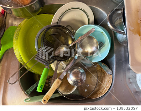 A dirty kitchen sink full of dirty dishes, pots and cutlery after cooking, cleaning up after housework and washing dishes A dirty kitchen sink full of dirty dishes, pots and cutlery after cooking, cleaning up after housework and washing dishes 139332057