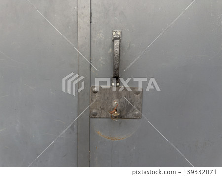Gray metal garage door with rusty lock and key, close up of industrial type security gate exposed to weather conditions 139332071