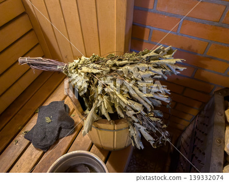 Dry birch sauna broom on a wooden bucket in a traditional steam bath, Belarusian banya accessories for spa and wellness Dry birch sauna broom on a wooden bucket in a traditional steam bath, Belarusian banya accessories for spa and wellness 139332074