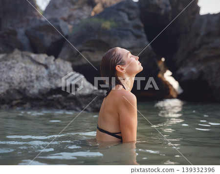 Young woman enjoying serene evening at sea in Krabi, Thailand during sunset. Calm waves, golden light, and peaceful atmosphere highlight tropical beauty and connection with nature. Young woman enjoying serene evening at sea in Krabi, Thailand during sunset. Calm waves, golden light, and peaceful atmosphere highlight tropical beauty and connection with nature. 139332396