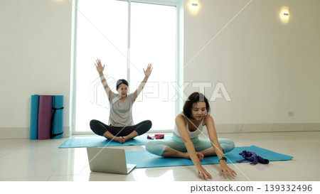 Two women practicing seated butterfly pose yoga with arm stretch and forward reach on mats during home workout, improving flexibility, hip opening and relaxation, promoting mindfulness and healthy Two women practicing seated butterfly pose yoga with arm stretch and forward reach on mats during home workout, improving flexibility, hip opening and relaxation, promoting mindfulness and healthy 139332496