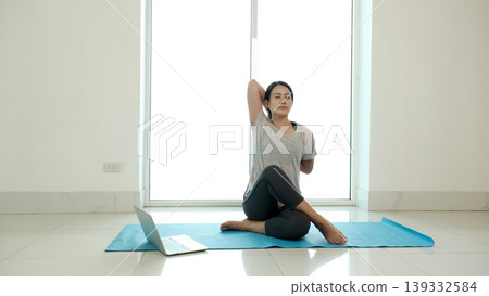 Woman practicing advanced seated yoga pose with arm stretch at home using laptop for online class, enhancing flexibility and posture, showcasing healthy lifestyle, fitness routine and digital wellness Woman practicing advanced seated yoga pose with arm stretch at home using laptop for online class, enhancing flexibility and posture, showcasing healthy lifestyle, fitness routine and digital wellness 139332584