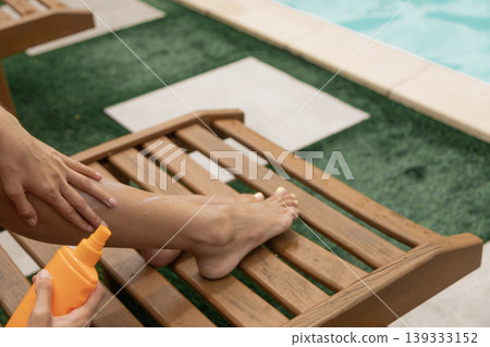 Person applying sun protection lotion on leg by swimming pool during summer relaxation. Person applying sun protection lotion on leg by swimming pool during summer relaxation. 139333152