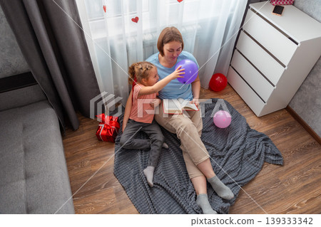 Top view of young Caucasian woman reads a book of fairy tales to her child. A preschool-age girl is interested in spending time with her mom. Family leisure and education Top view of young Caucasian woman reads a book of fairy tales to her child. A preschool-age girl is interested in spending time with her mom. Family leisure and education 139333342