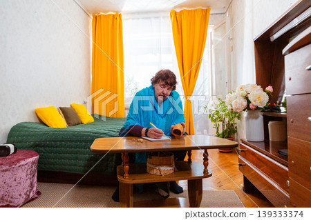 Older Caucasian woman using dice for a game at a table indoors. Quiet moment and concentration. Concept of pastime and comfort. Wide shot Older Caucasian woman using dice for a game at a table indoors. Quiet moment and concentration. Concept of pastime and comfort. Wide shot 139333374