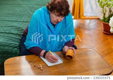 Senior female playing dice game in a cozy room. Leisure activity and engagement. Concept of happiness and aging lifestyle. Senior female playing dice game in a cozy room. Leisure activity and engagement. Concept of happiness and aging lifestyle. 139333375