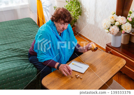 Older woman sitting at a table and playing a classic dice game. Quiet indoor setting and focus. Concept of hobby and retirement life. Older woman sitting at a table and playing a classic dice game. Quiet indoor setting and focus. Concept of hobby and retirement life. 139333376
