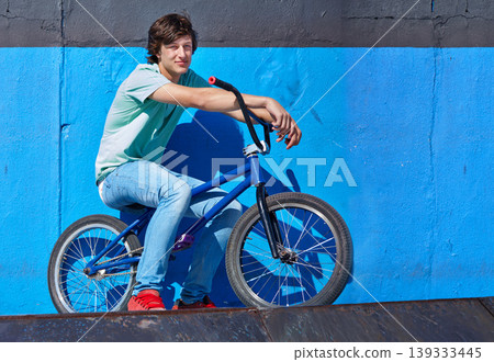 Wall, bicycle and portrait of boy teenager riding for fitness, health or wellness in the road. Smile, sports and young man cycling on bike for transportation, adventure and adrenaline for practice. Wall, bicycle and portrait of boy teenager riding for fitness, health or wellness in the road. Smile, sports and young man cycling on bike for transportation, adventure and adrenaline for practice. 139333445