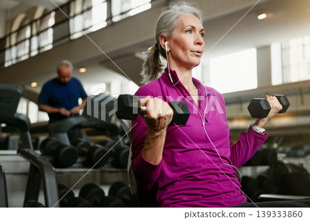 Dumbbell, fitness and senior woman at a gym for training, wellness and cardio with earphones, music or mindset. Weightlifting, bodybuilding and elderly female person at sports center for arm workout 139333860