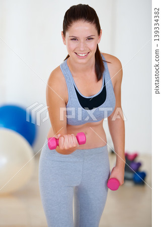 Woman, flexing or portrait with dumbbells in gym, health glow or fitness for weight loss with exercise. Young person, happy and face with hand weights for training wellness in sports clothes Woman, flexing or portrait with dumbbells in gym, health glow or fitness for weight loss with exercise. Young person, happy and face with hand weights for training wellness in sports clothes 139334382