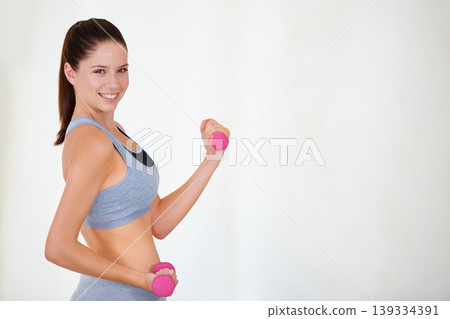 Woman, flex or portrait with dumbbells in studio, health wellness or fitness action for weight loss with exercise. Young person, pride and face with hand weights for tone muscle by white background Woman, flex or portrait with dumbbells in studio, health wellness or fitness action for weight loss with exercise. Young person, pride and face with hand weights for tone muscle by white background 139334391