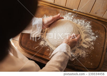 Female baker rubbing flour to the bread dough before baking it in the oven. Preparing tasty bread at home Female baker rubbing flour to the bread dough before baking it in the oven. Preparing tasty bread at home 139334456