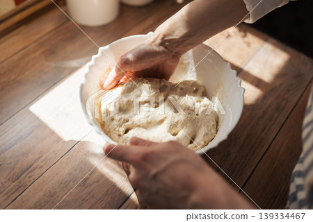 Girl knead dough for baking bread in a plate. Sunny morning in the kitchen, girl hostess baking homemade bread 139334467