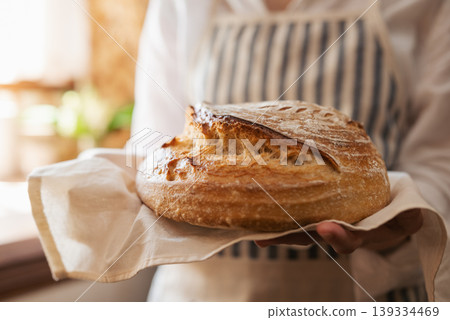 Close up of a hostess holding traditional ukrainian bread just baked from the oven. Self made bread in hands of a girl standing in kitchen Close up of a hostess holding traditional ukrainian bread just baked from the oven. Self made bread in hands of a girl standing in kitchen 139334469