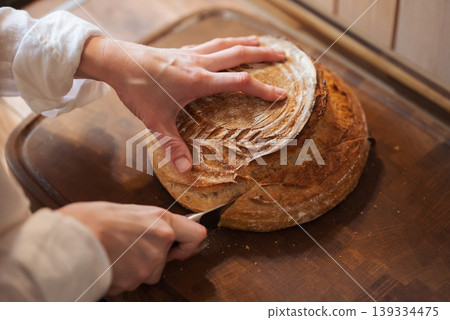 Hands of a girl cutting homemade bread on wooden tray. Baking bread at home, cutting fresh aromatic loan of bread Hands of a girl cutting homemade bread on wooden tray. Baking bread at home, cutting fresh aromatic loan of bread 139334475