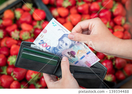 Girl buying strawberry at the market and taking 200 hryvnias from the purse. Buying strawberry at market in Spring Girl buying strawberry at the market and taking 200 hryvnias from the purse. Buying strawberry at market in Spring 139334488