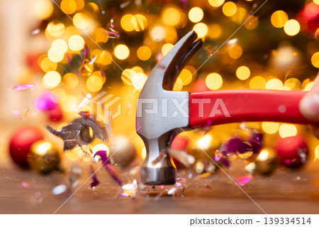 Shattering christmas ball decoration with hammer. Christmas background, breaking glass decoration, lack of christmas mood concept Shattering christmas ball decoration with hammer. Christmas background, breaking glass decoration, lack of christmas mood concept 139334514