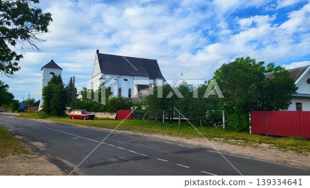 The 16th-century Catholic Church of the Holy Trinity in the Belarusian agro-town of Chernavchitsy Brest, a red car on a village road, architectural history study, rural travel spirit. The 16th-century Catholic Church of the Holy Trinity in the Belarusian agro-town of Chernavchitsy Brest, a red car on a village road, architectural history study, rural travel spirit. 139334641