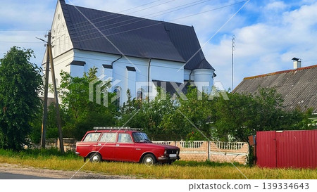 The 16th-century Catholic Church of the Holy Trinity in the Belarusian agro-town of Chernavchitsy Brest, a red car on a village road, architectural history study, rural travel spirit. The 16th-century Catholic Church of the Holy Trinity in the Belarusian agro-town of Chernavchitsy Brest, a red car on a village road, architectural history study, rural travel spirit. 139334643