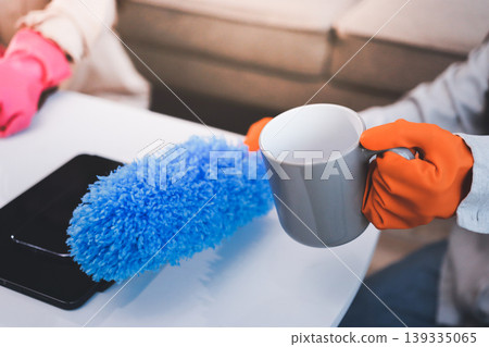 Person cleaning the room, cleaning staff is using cloth and spraying disinfectant to wipe the tables in the company office room. Cleaning staff. Maintaining cleanliness in the organization. 139335065