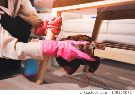 Person cleaning the room, cleaning staff is using cloth and spraying disinfectant to wipe the tables in the company office room. Cleaning staff. Maintaining cleanliness in the organization. 139335072