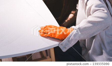 Person cleaning the room, cleaning staff is using cloth and spraying disinfectant to wipe the tables in the company office room. Cleaning staff. Maintaining cleanliness in the organization. Person cleaning the room, cleaning staff is using cloth and spraying disinfectant to wipe the tables in the company office room. Cleaning staff. Maintaining cleanliness in the organization. 139335090