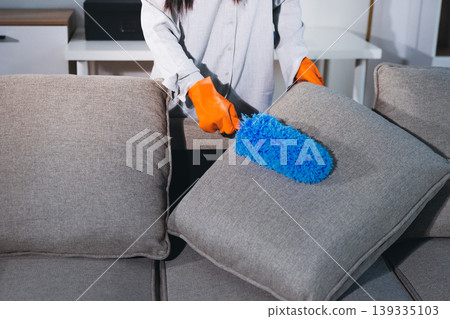 Person cleaning the room, cleaning staff is using cloth and spraying disinfectant to wipe the tables in the company office room. Cleaning staff. Maintaining cleanliness in the organization. 139335103