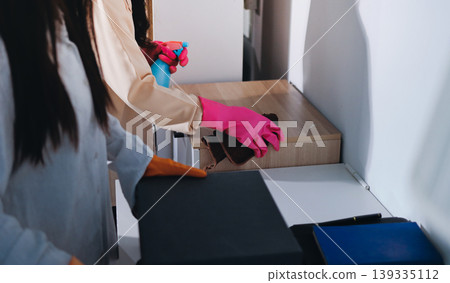 Person cleaning the room, cleaning staff is using cloth and spraying disinfectant to wipe the tables in the company office room. Cleaning staff. Maintaining cleanliness in the organization. Person cleaning the room, cleaning staff is using cloth and spraying disinfectant to wipe the tables in the company office room. Cleaning staff. Maintaining cleanliness in the organization. 139335112