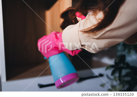 Person cleaning the room, cleaning staff is using cloth and spraying disinfectant to wipe the tables in the company office room. Cleaning staff. Maintaining cleanliness in the organization. Person cleaning the room, cleaning staff is using cloth and spraying disinfectant to wipe the tables in the company office room. Cleaning staff. Maintaining cleanliness in the organization. 139335120