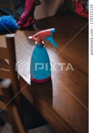 Person cleaning the room, cleaning staff is using cloth and spraying disinfectant to wipe the tables in the company office room. Cleaning staff. Maintaining cleanliness in the organization. Person cleaning the room, cleaning staff is using cloth and spraying disinfectant to wipe the tables in the company office room. Cleaning staff. Maintaining cleanliness in the organization. 139335126
