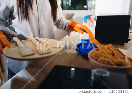 Person cleaning the room, cleaning staff is using cloth and spraying disinfectant to wipe the tables in the company office room. Cleaning staff. Maintaining cleanliness in the organization. Person cleaning the room, cleaning staff is using cloth and spraying disinfectant to wipe the tables in the company office room. Cleaning staff. Maintaining cleanliness in the organization. 139335131