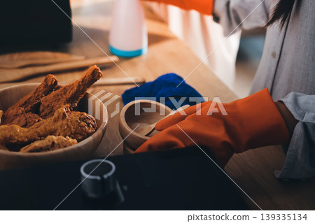 Person cleaning the room, cleaning staff is using cloth and spraying disinfectant to wipe the tables in the company office room. Cleaning staff. Maintaining cleanliness in the organization. 139335134