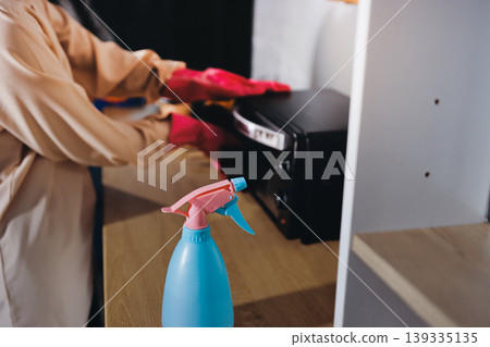 Person cleaning the room, cleaning staff is using cloth and spraying disinfectant to wipe the tables in the company office room. Cleaning staff. Maintaining cleanliness in the organization. Person cleaning the room, cleaning staff is using cloth and spraying disinfectant to wipe the tables in the company office room. Cleaning staff. Maintaining cleanliness in the organization. 139335135