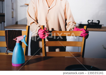 Person cleaning the room, cleaning staff is using cloth and spraying disinfectant to wipe the tables in the company office room. Cleaning staff. Maintaining cleanliness in the organization. Person cleaning the room, cleaning staff is using cloth and spraying disinfectant to wipe the tables in the company office room. Cleaning staff. Maintaining cleanliness in the organization. 139335141
