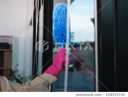 Person cleaning the room, cleaning staff is using cloth and spraying disinfectant to wipe the tables in the company office room. Cleaning staff. Maintaining cleanliness in the organization. 139335142