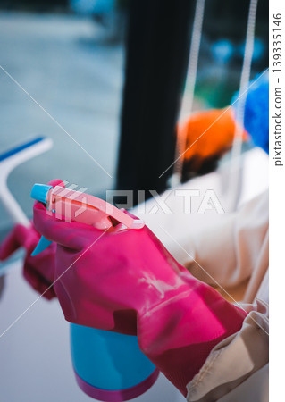 Person cleaning the room, cleaning staff is using cloth and spraying disinfectant to wipe the tables in the company office room. Cleaning staff. Maintaining cleanliness in the organization. 139335146